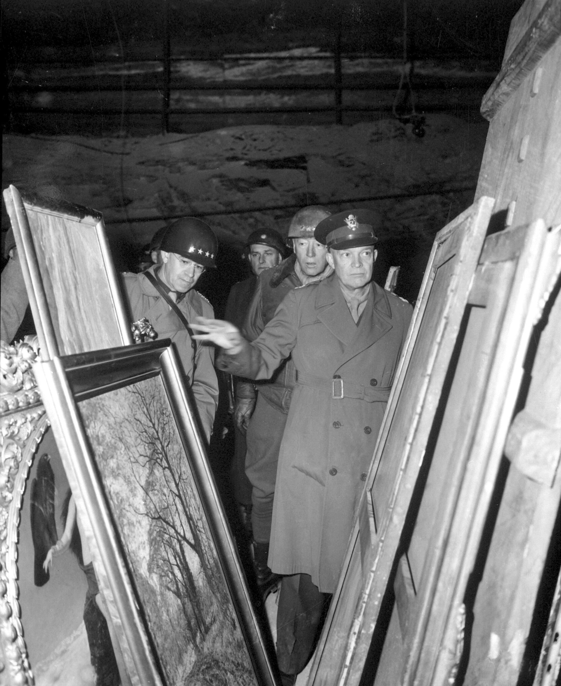 General Dwight D. Eisenhower, with General Omar N. Bradley behind him at left and Lieutenant General George S. Patton at right, among framed paintings stored in the Merkers salt mine in Thuringia, photographed by Lieutenant Moore of the United States Army on 12 April 1945, National Archives 111-SC-204516. The mine held Reichsbank gold and the evacuated holdings of the Berlin museums; the Nefertiti bust had been brought here the previous month and went on from Frankfurt to the Wiesbaden Central Collecting Point in August 1945.