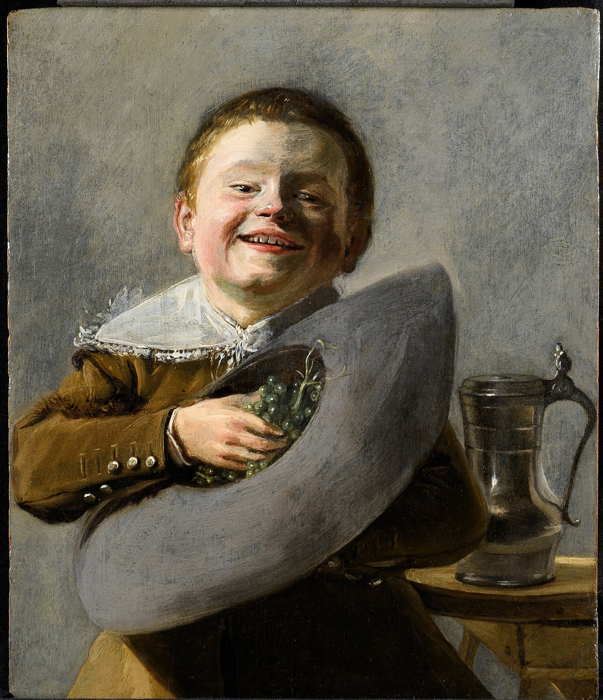 A laughing boy with grapes in his hat