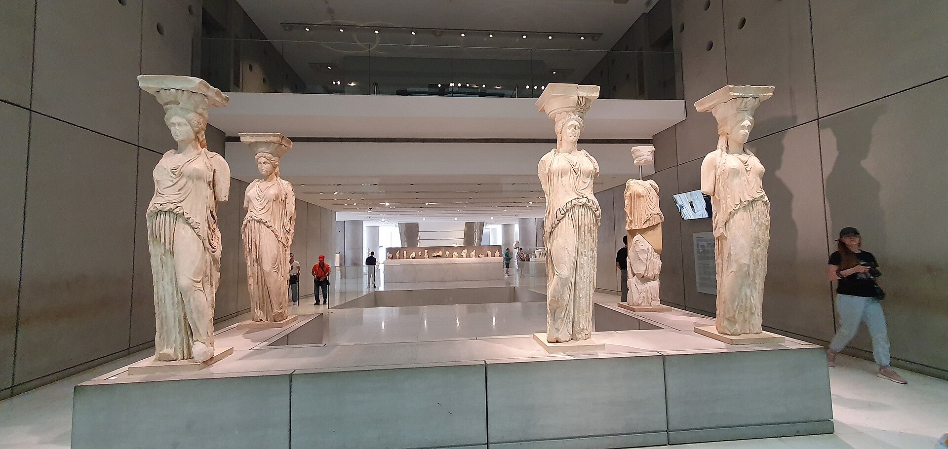 Five marble caryatid statues in their original south-porch arrangement, standing on a low platform inside a windowless gallery