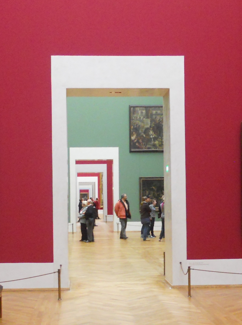 A red-walled gallery room hung with small dark-toned Flemish and Dutch paintings