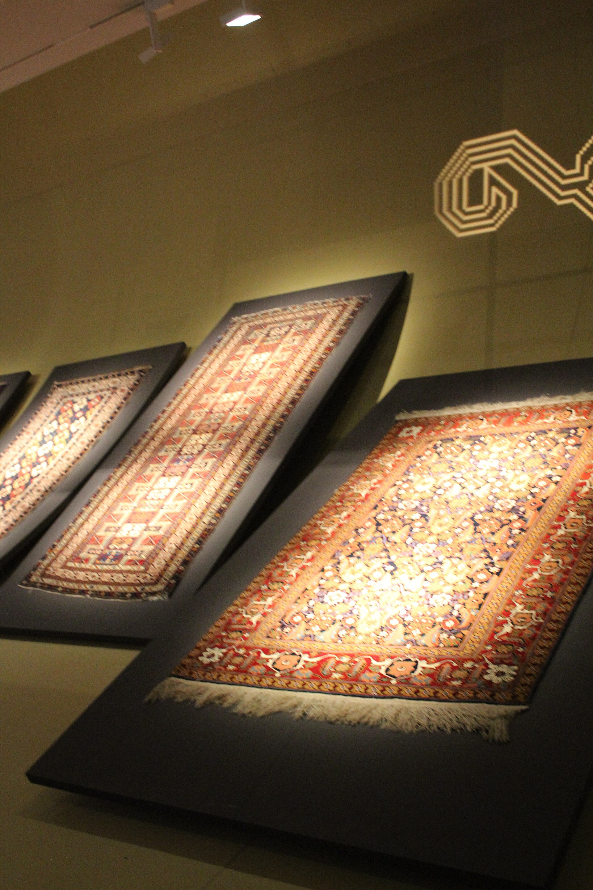 Pile carpets in patterned medallion designs displayed at an angle in a gallery