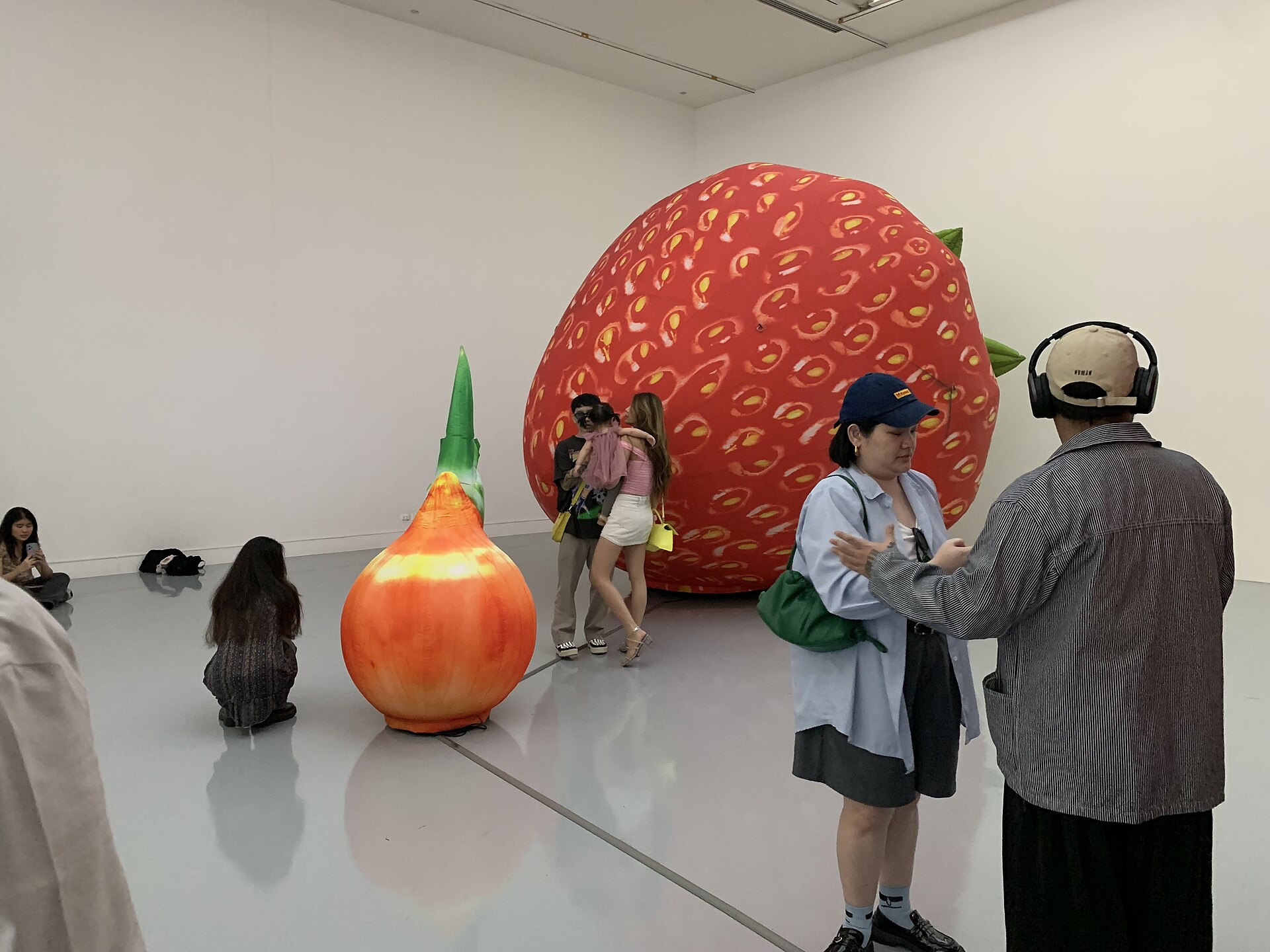 A curved gallery wall hung with a row of Buddhist scroll paintings inside one of BACC's exhibition galleries, visitors viewing from a polished floor, during Bangkok Art Biennale 2024