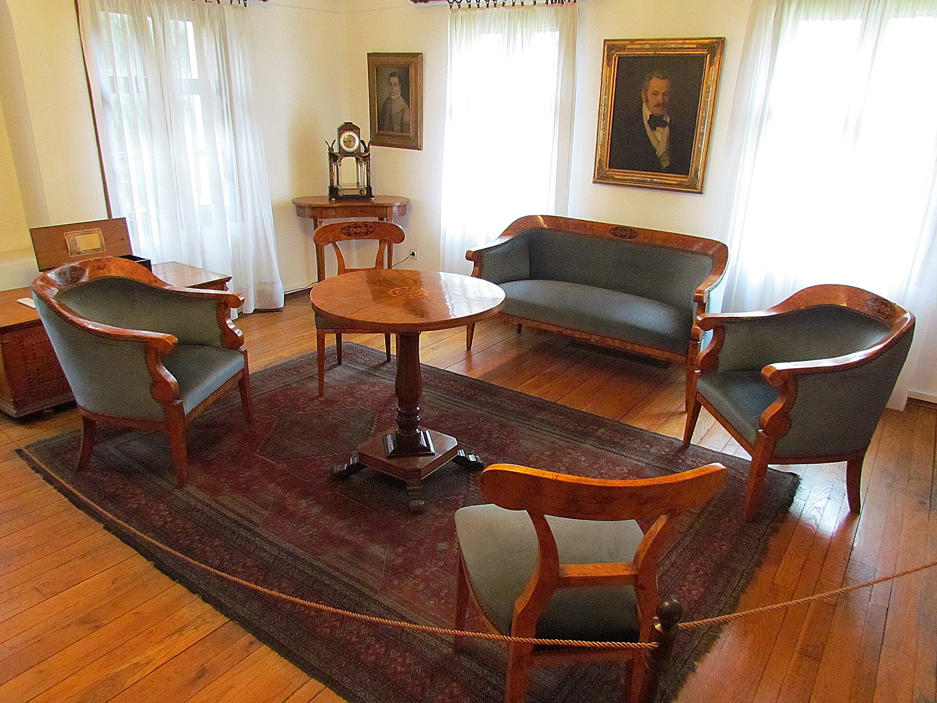 A Biedermeier-furnished drawing room with a curved sofa, armchairs and family portraits