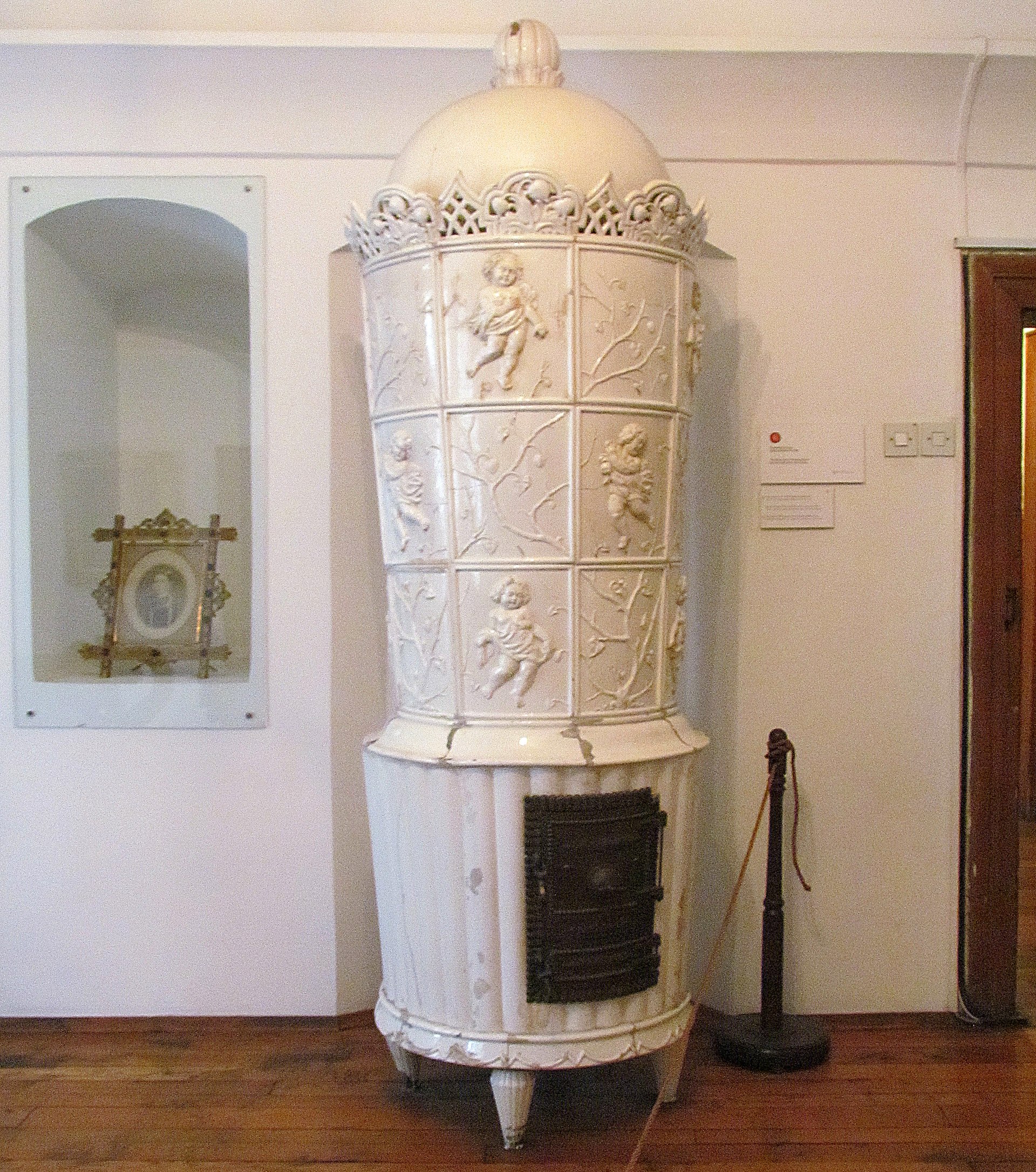 A tall white glazed ceramic stove with cherub-relief tiles, standing in a period room
