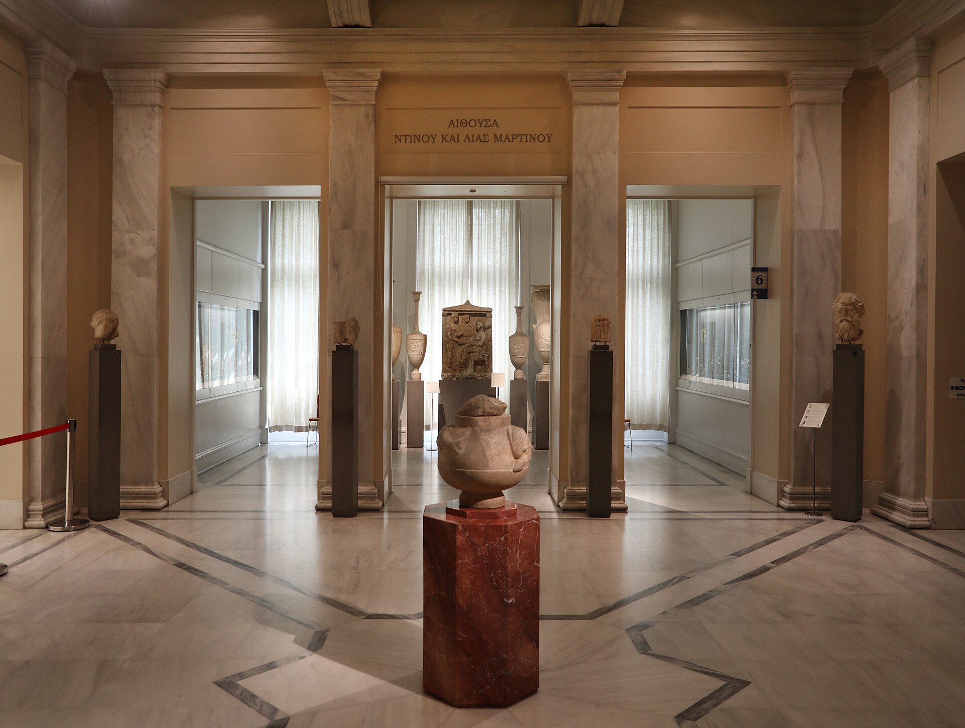 A ground-floor gallery of the Benaki Museum, ancient sculpture and vessels on marble plinths beneath a colonnaded ceiling