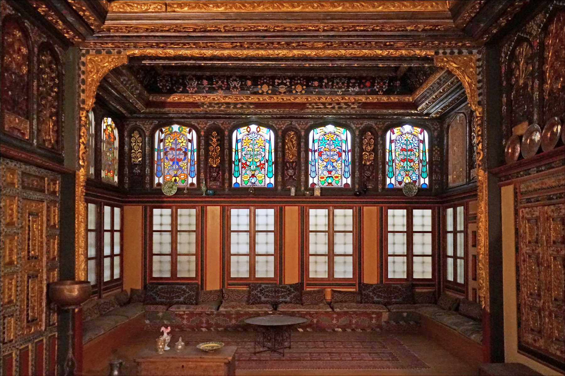 The reconstructed eighteenth-century reception room from a Kozani mansion, its walls and coffered ceiling entirely carved and gilded, with stained-glass windows and a raised seating platform