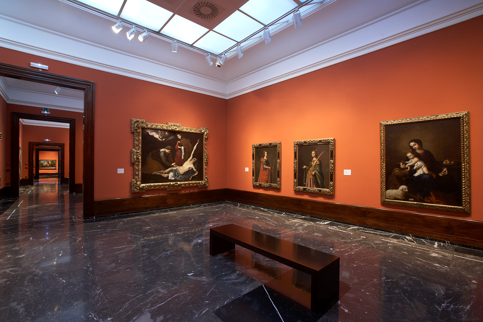 A gallery room hung with dark-toned old master paintings on terracotta-coloured walls