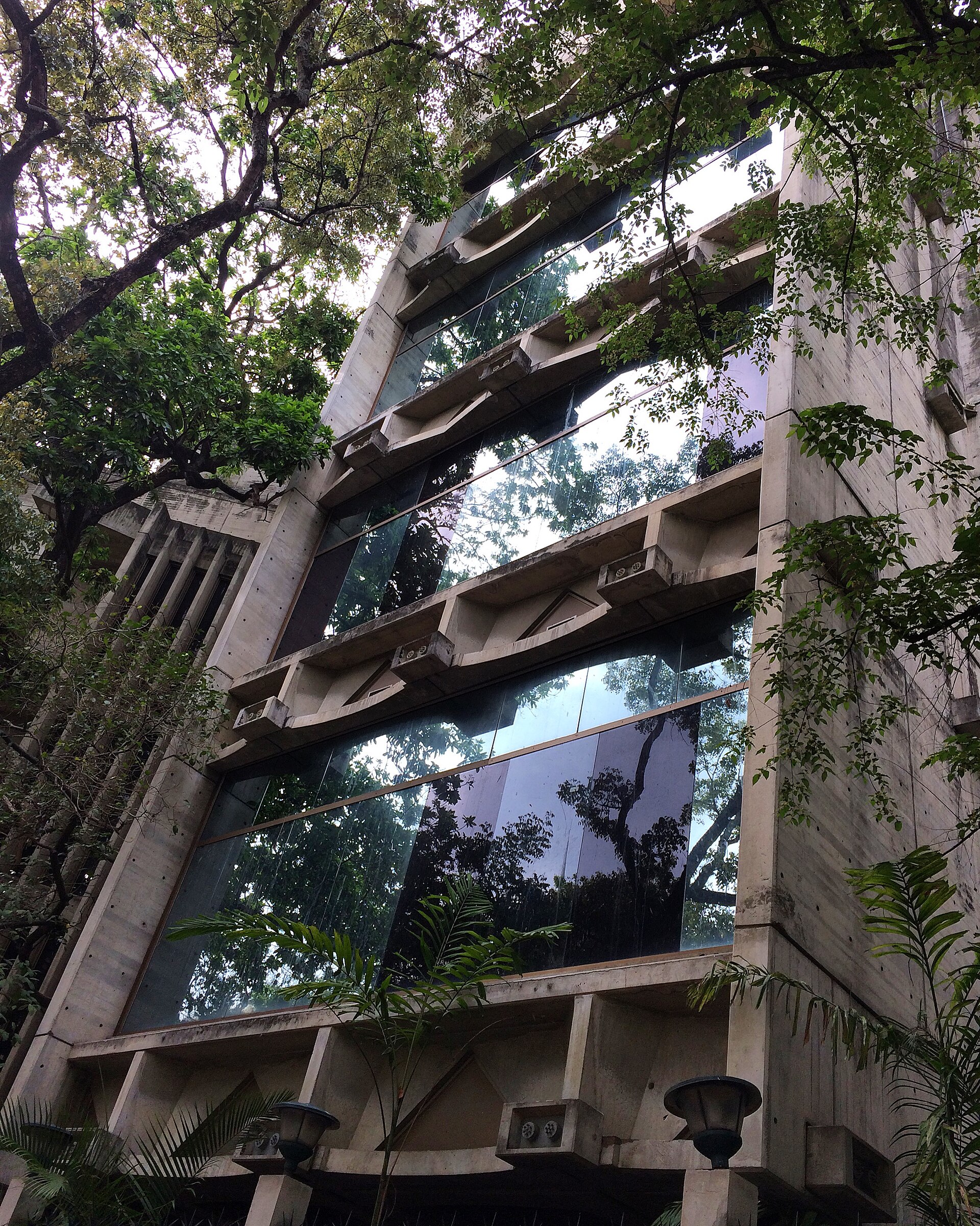 Upward view of the modern brutalist wing's precast concrete frame and mirrored glass, seen through surrounding trees