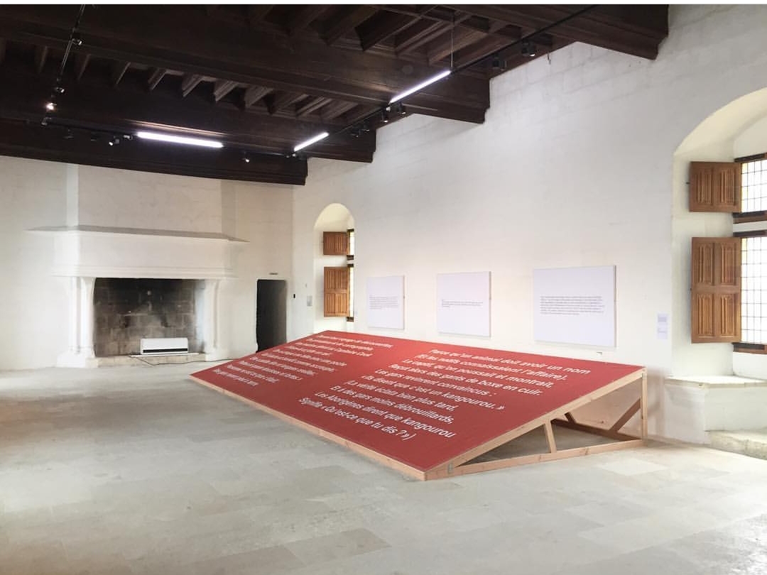 A whitewashed exhibition room in the museum, with an old fireplace and a text-based Art & Language installation on the floor