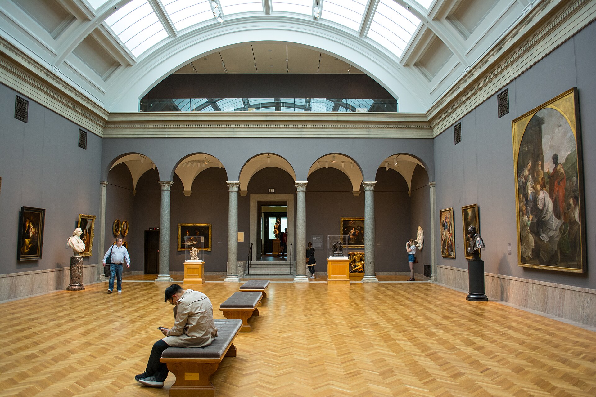 A skylit European painting hall with an arcaded screen at the far end