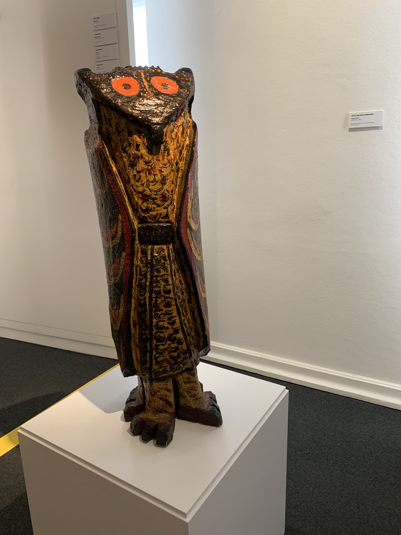 A carved and painted wooden sculpture on a plinth inside the museum