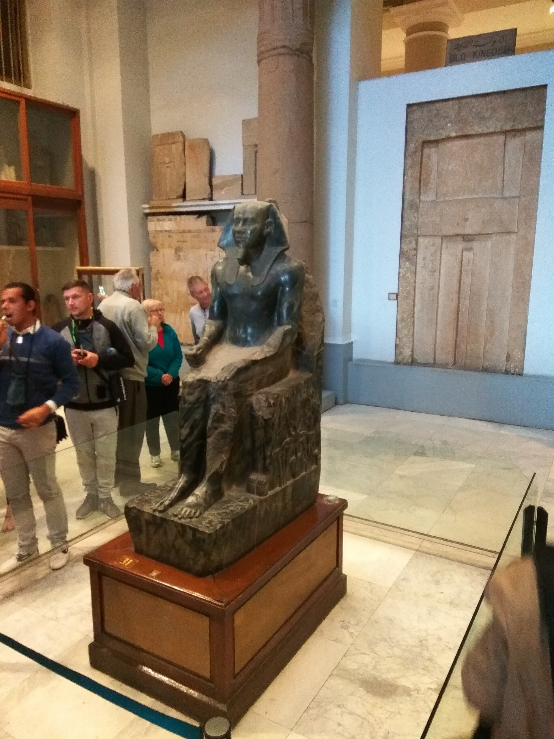 The seated statue of Khafre in an Old Kingdom room, with a mastaba false door behind it