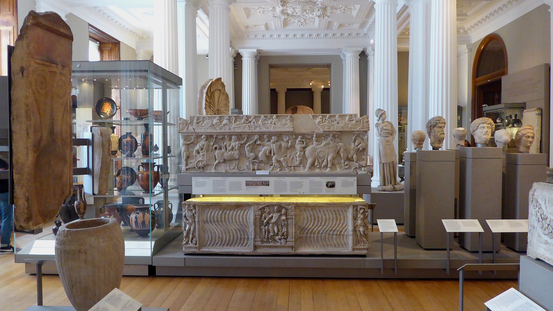 The Classical Archaeology Gallery, with a large carved Roman marble sarcophagus, Greek and Roman portrait busts on plinths, and painted Greek pottery in wall cases beneath a coffered and coffer-lit ceiling
