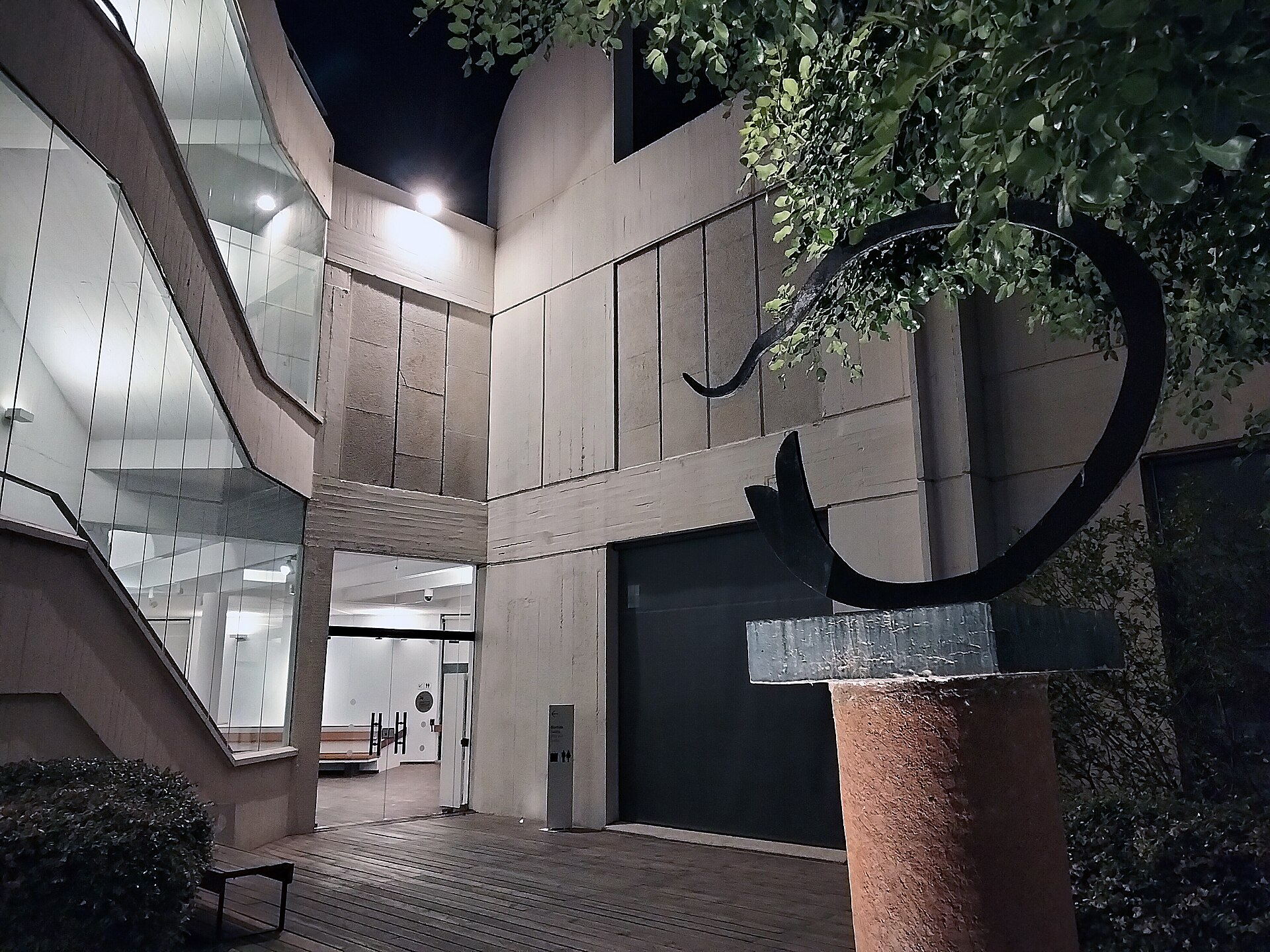 One of the Fundacio's interior courtyards at night, glass and exposed white concrete around a paved yard with a metal sculpture
