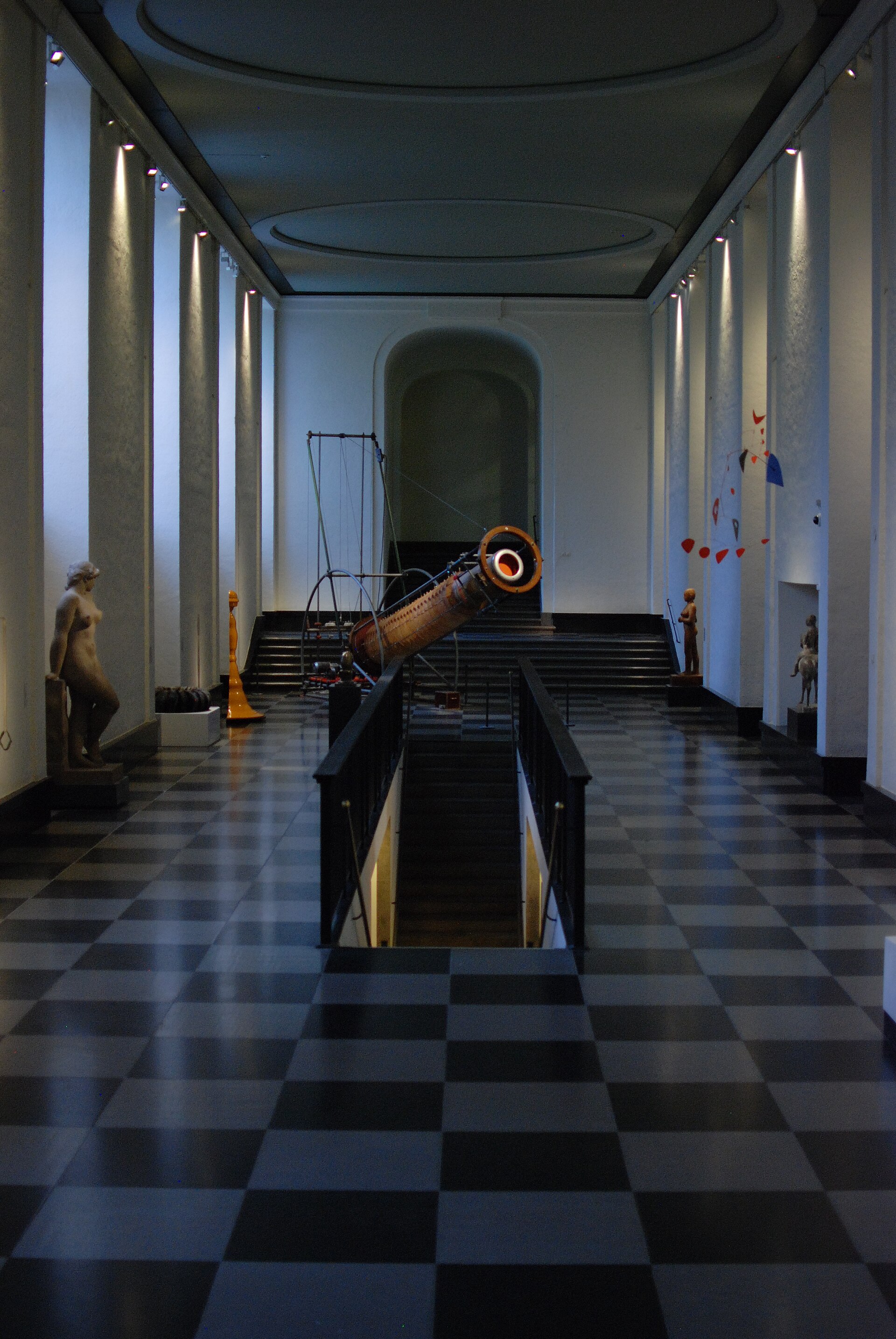 A long museum hall with a black-and-white checkered floor lined with sculptures on plinths