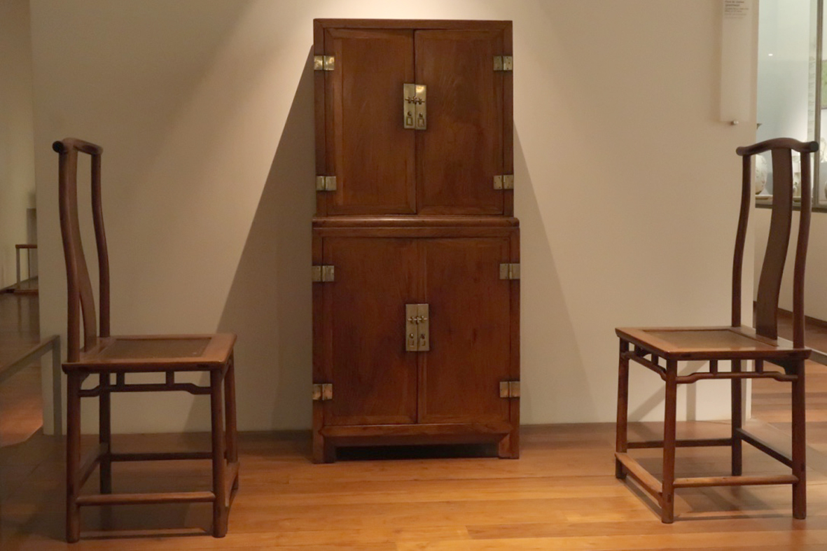 A Ming-dynasty rosewood cabinet flanked by a pair of chairs, on display in a gallery of the museum's Chinese furniture collection