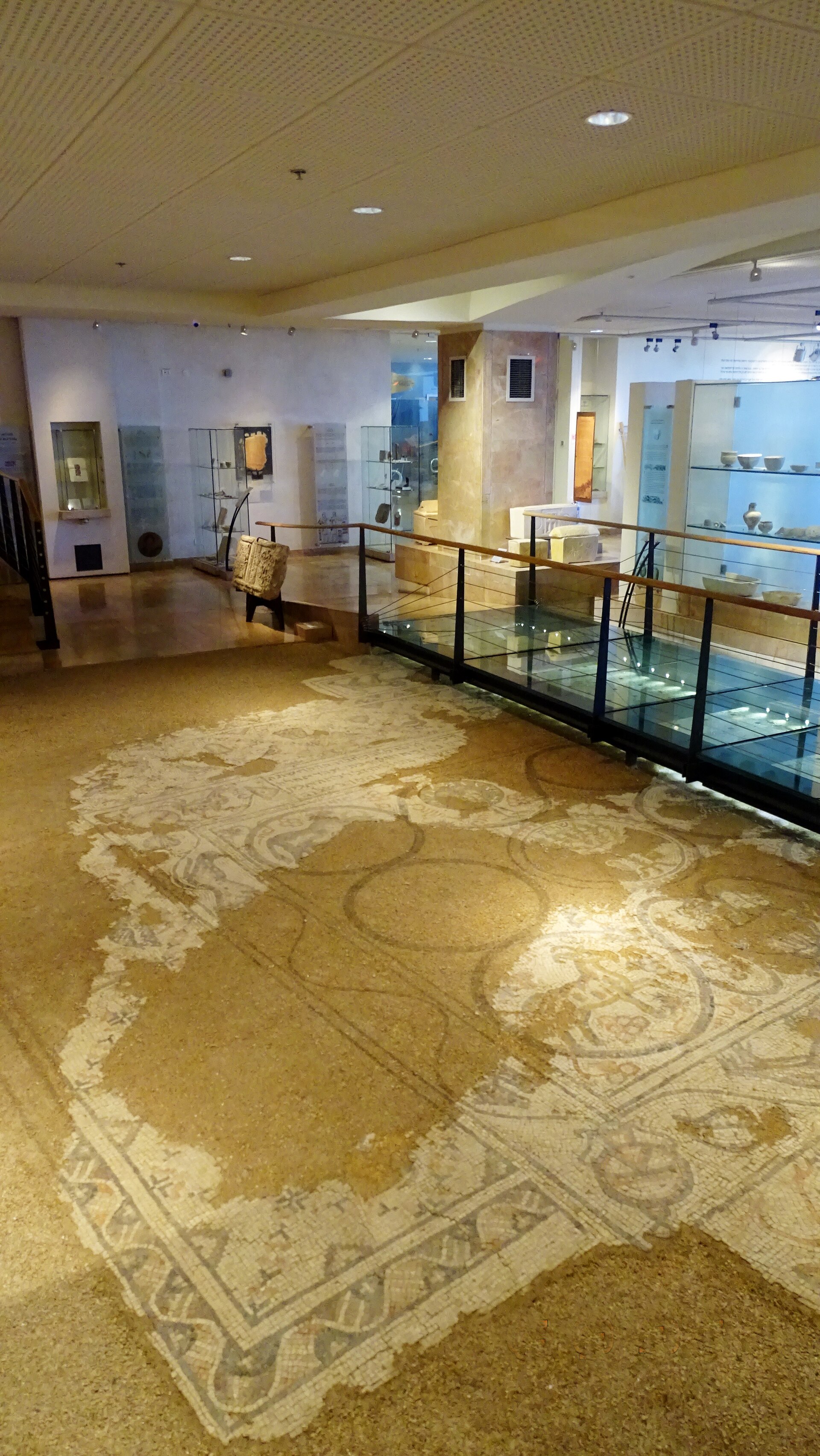 A reconstructed section of ancient stone fortification wall beside a full-size working replica of a wooden torsion siege engine (ballista), displayed on the museum floor among glass exhibition cases