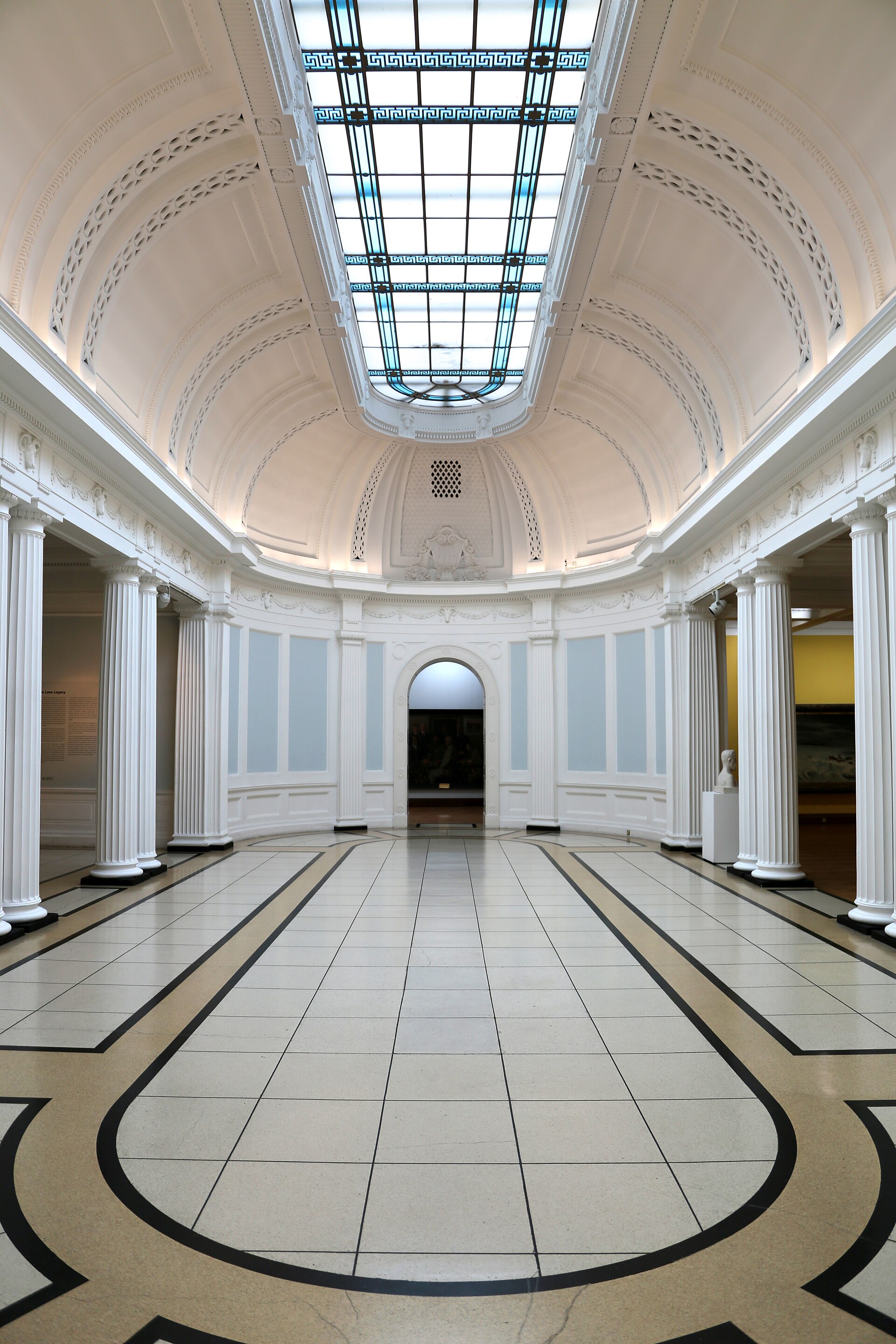 A top-lit, colonnaded oval room in the gallery's historic wing, with a coffered vaulted ceiling and a glazed oculus