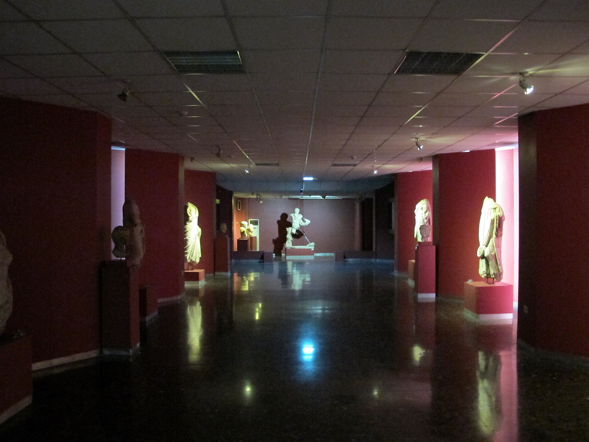 A red-walled gallery corridor lined with marble statues and portrait busts on pedestals