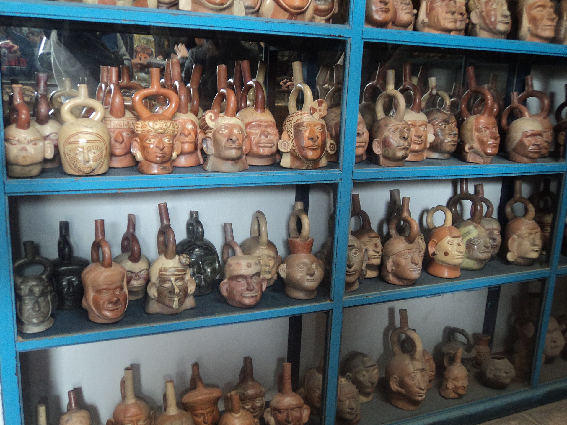 A glass-fronted shelf of Moche portrait vessels, ceramic jars modelled as individual human heads, on display at Museo Larco