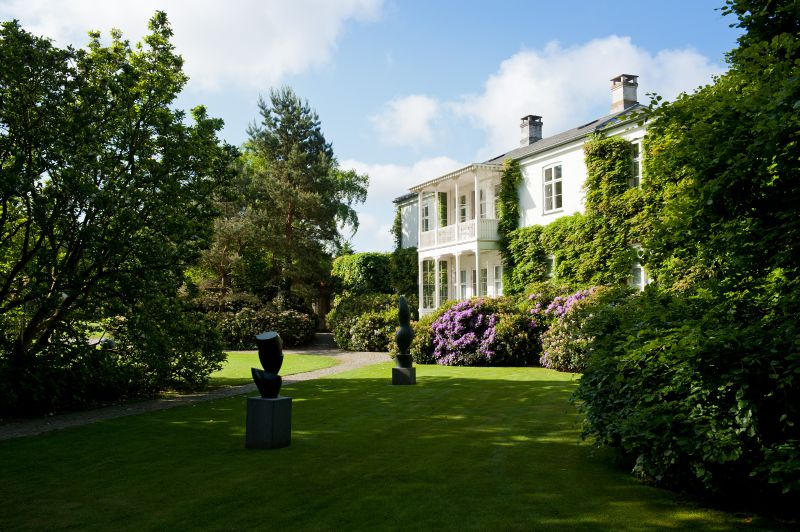 The ivy-covered old villa seen across the lawn, with two sculptures on the grass in front of it