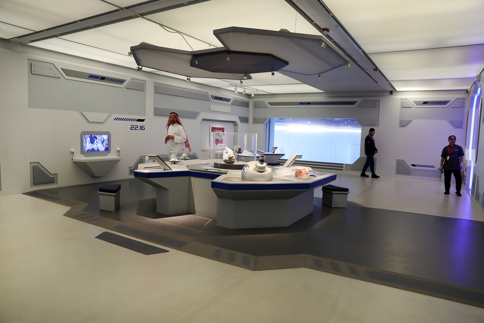 A futuristic space-themed exhibit room with curved consoles, screens and models, laid out for children