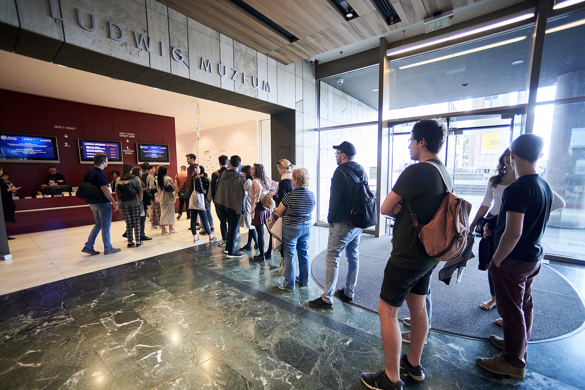 Visitors queuing at the Ludwig Museum ticket desk inside the Mupa Budapest lobby, with the museum's name lettered on the wall above