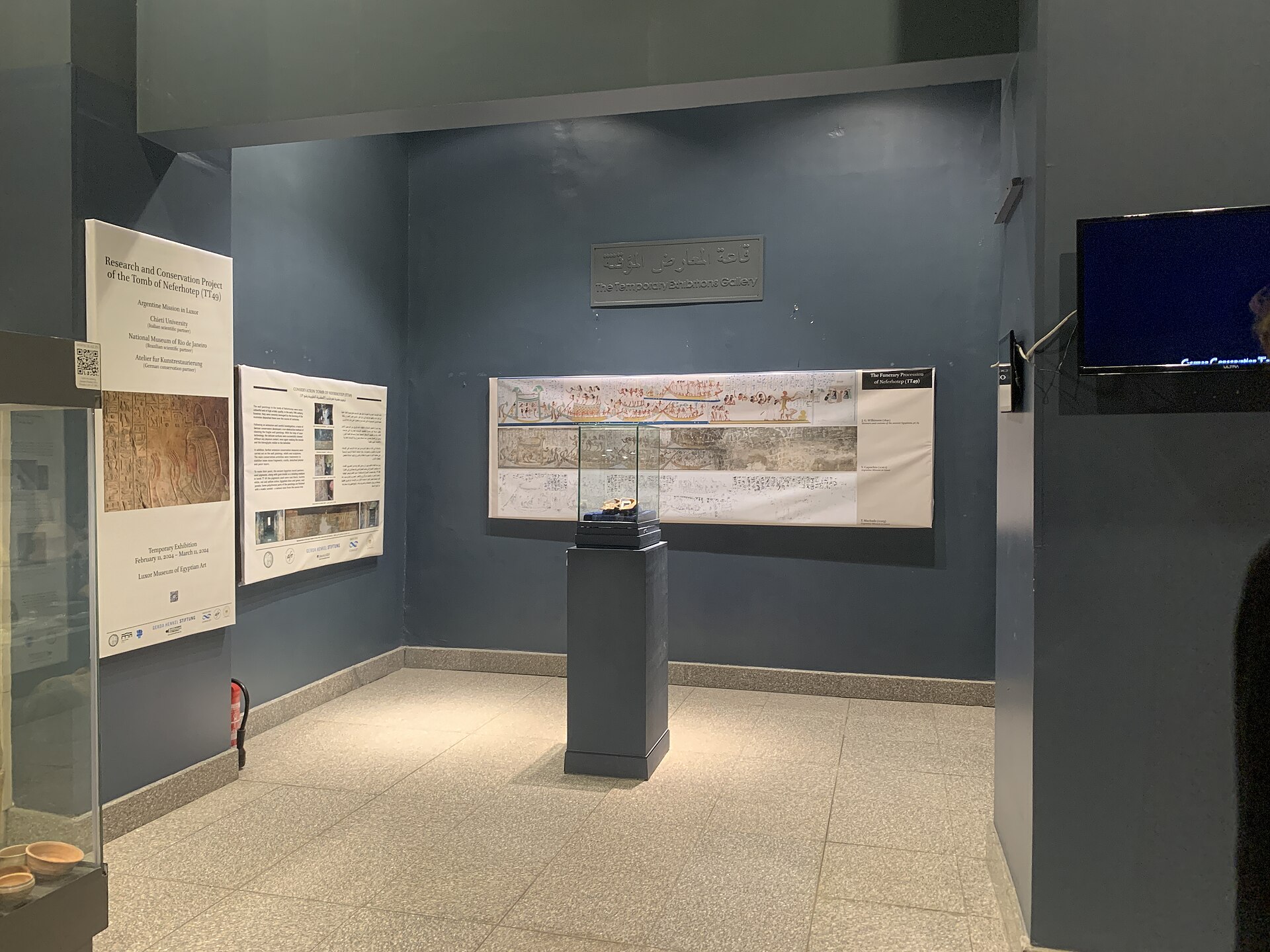 A darkened exhibition room with wall panels and a lit display case describing a tomb conservation project