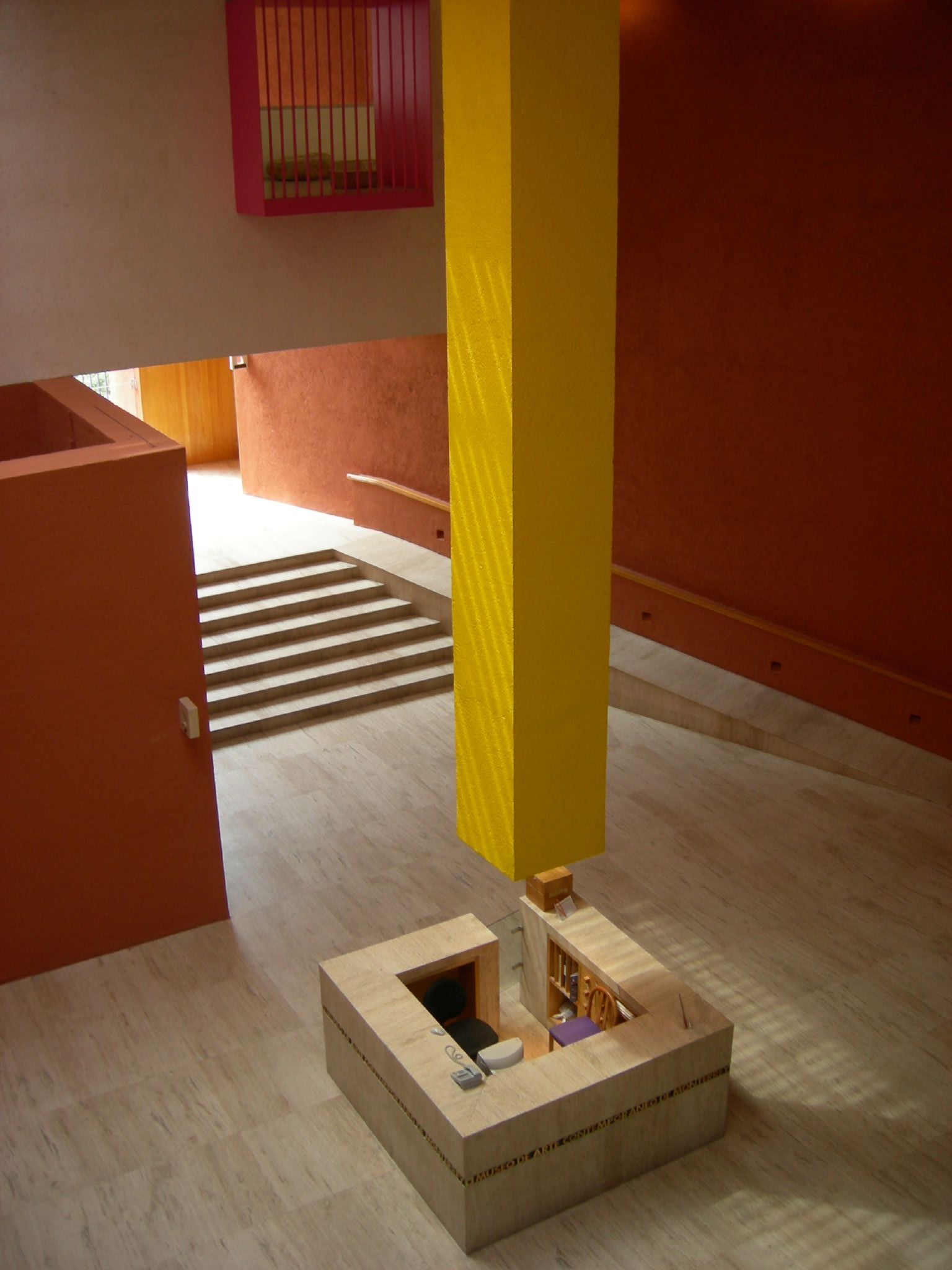 The information desk beneath a tall yellow column in the entrance vestibule, with a staircase and orange walls behind it