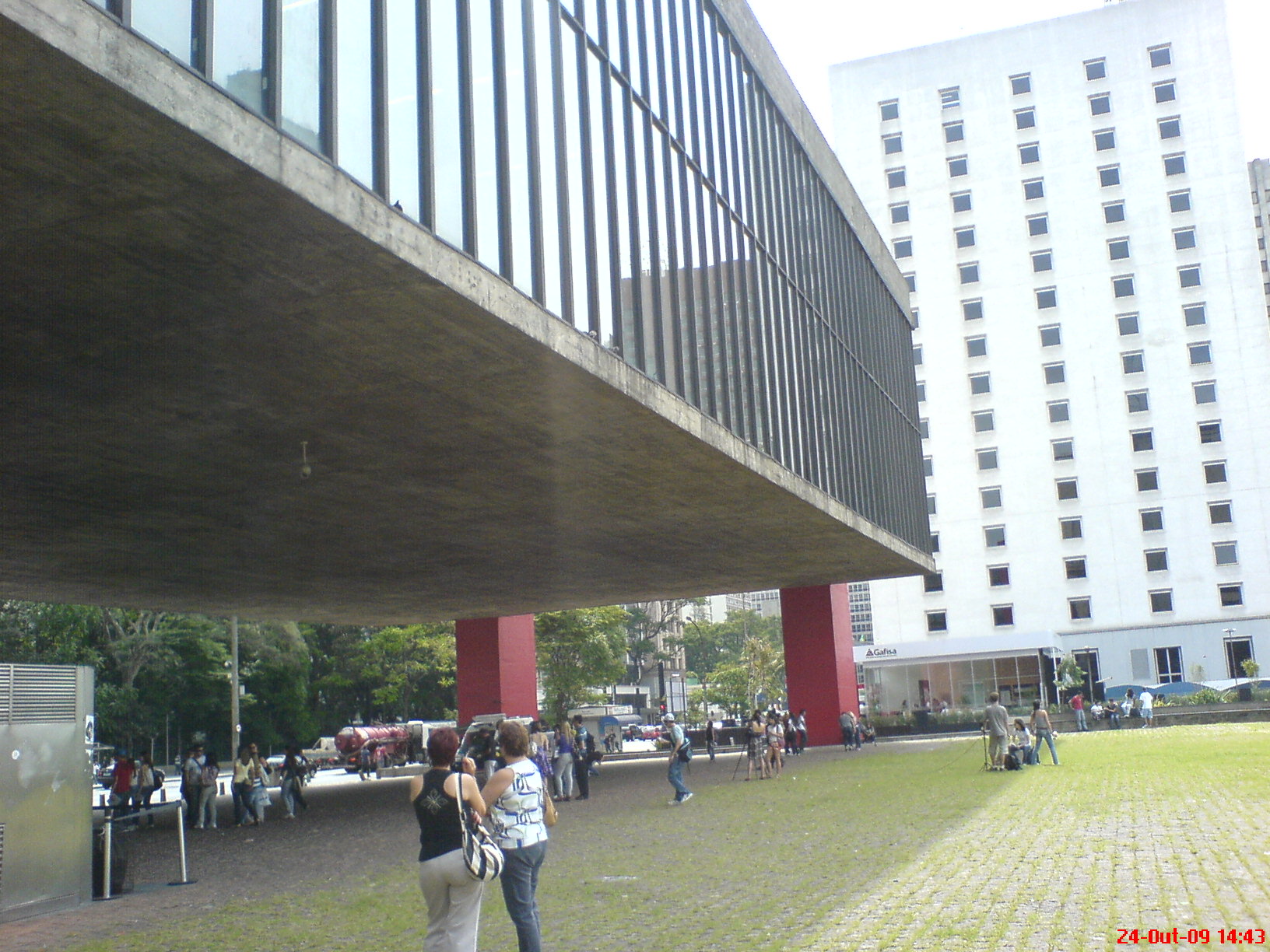 The open plaza beneath the suspended gallery block, with the red piers and the underside of the concrete beam