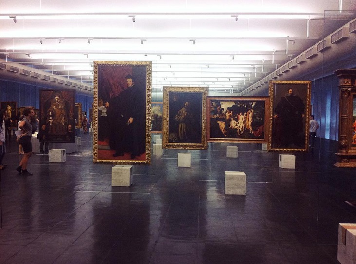 Paintings standing on concrete-and-glass easels in an open hall, with no dividing walls
