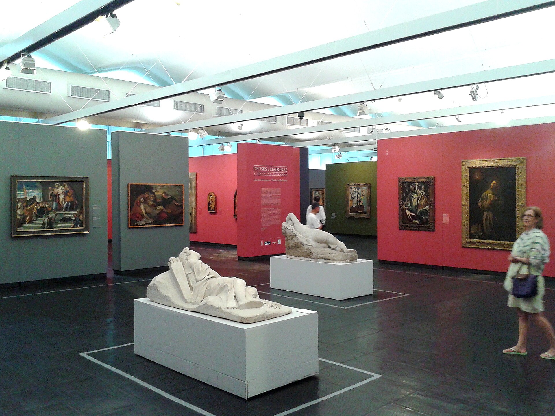 A partitioned temporary exhibition gallery with coloured walls, framed paintings and sculpture on plinths