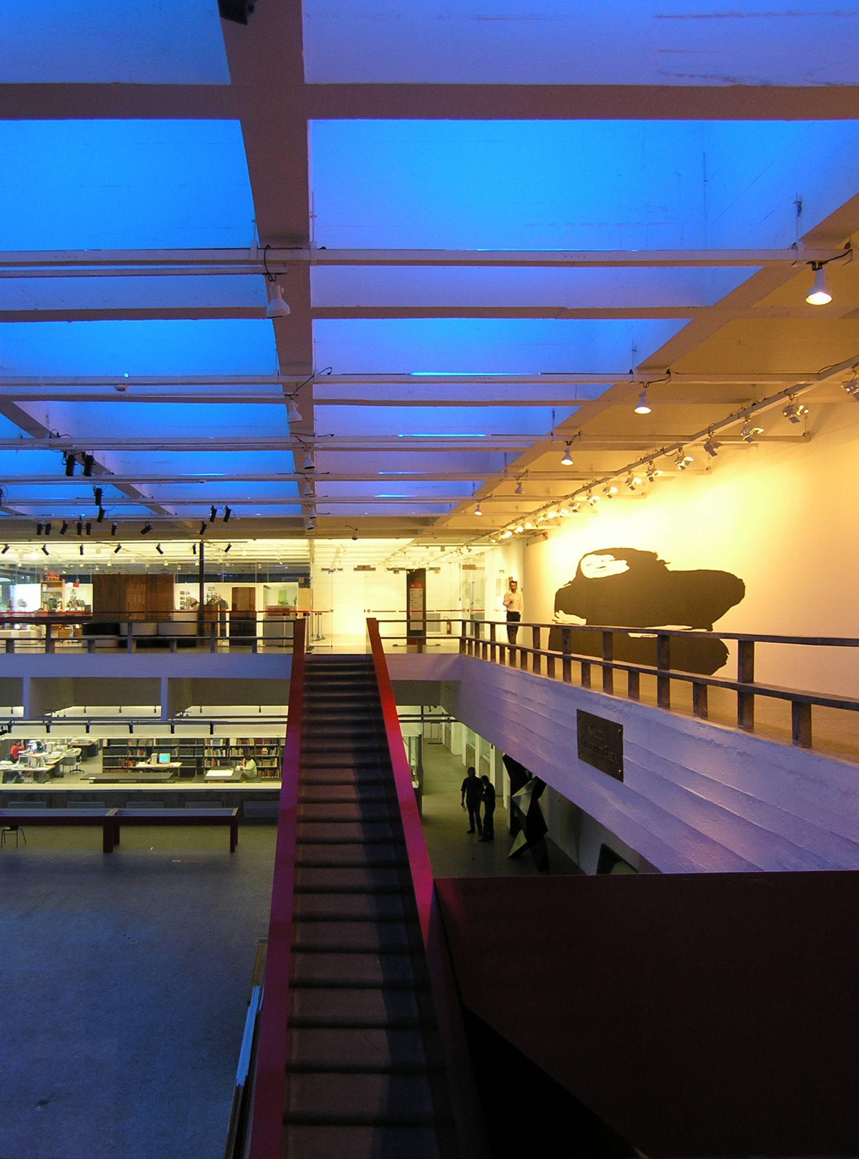 A basement level at MASP, with library reading tables and shelving below a gallery balcony
