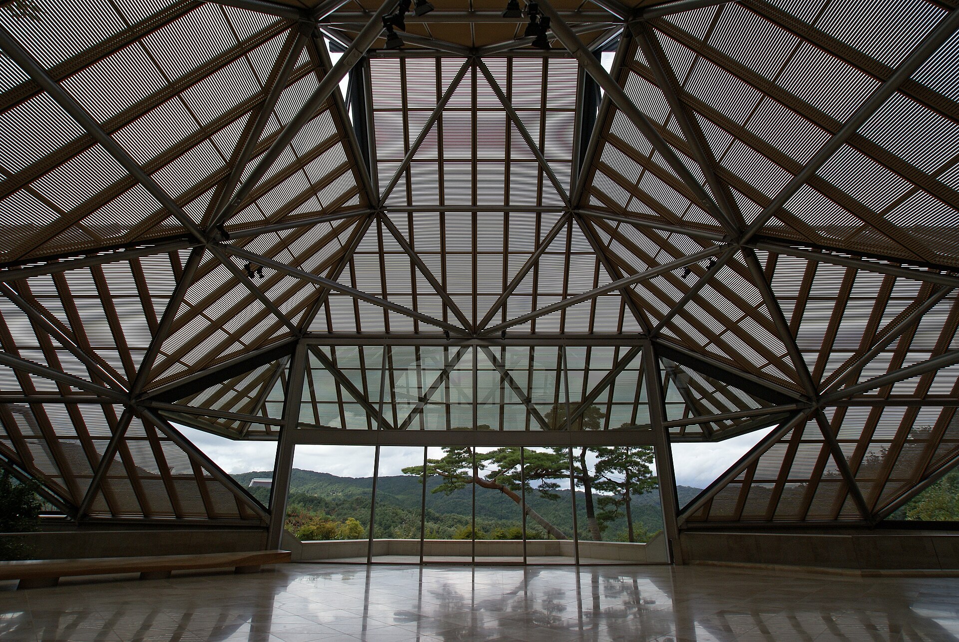 The triangulated glass-and-steel roof of the Miho Museum entrance hall, seen from inside with the surrounding hills visible through the glazing