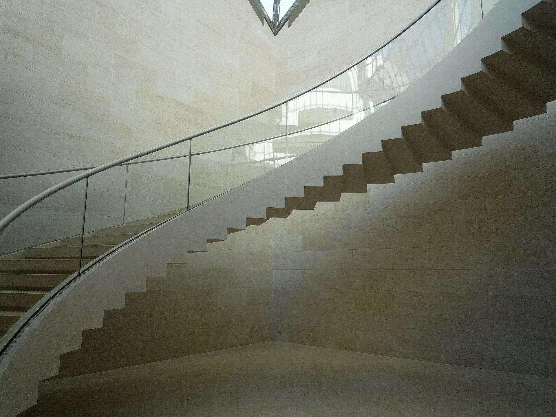 A wide stone staircase inside Mudam, rising between exhibition levels beneath a glass roof