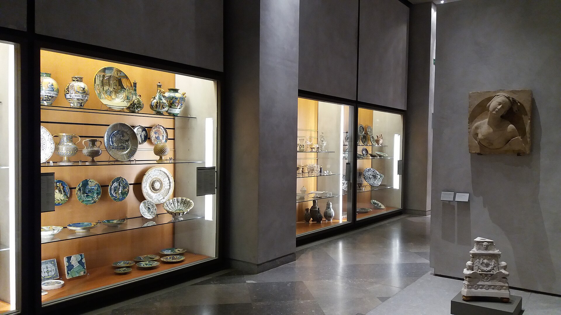 Lit display cases of Islamic and European ceramic plates, jugs and bowls along a gallery wall.