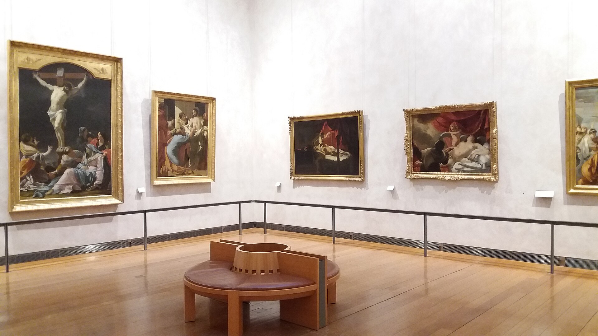 A gallery of large gilt-framed seventeenth-century religious paintings around a central circular bench.