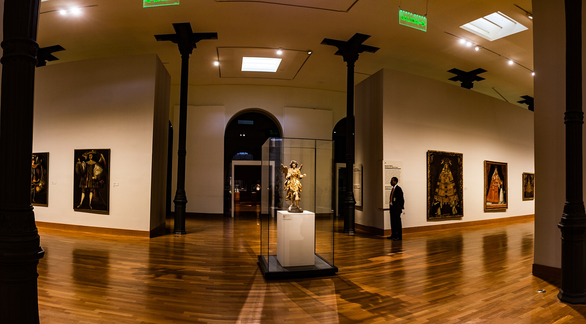 A gallery in MALI's Colonial Art Room, with colonial paintings on the walls and a gilded polychrome devotional sculpture in a glass case