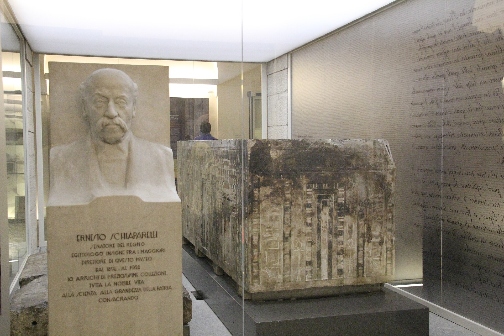 A marble bust of Ernesto Schiaparelli, the museum's director from 1894 to 1928, beside a large inscribed sarcophagus lid near the papyrus displays