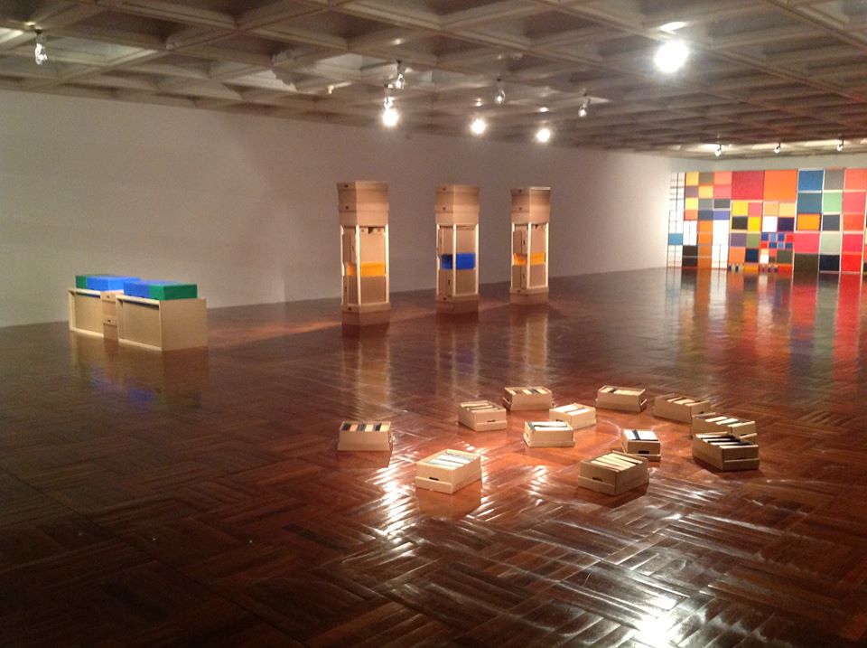 An installation of geometric painted panels and wooden crates on the parquet floor of Room 5, under its coffered ceiling