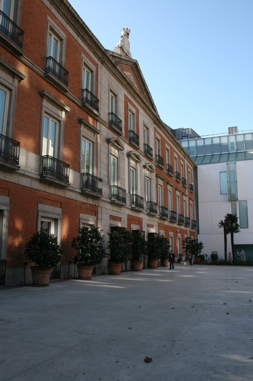 The rear courtyard of the palace, its brick and stone facade with a balustraded pediment set against the plain glazed wall of the modern extension behind it