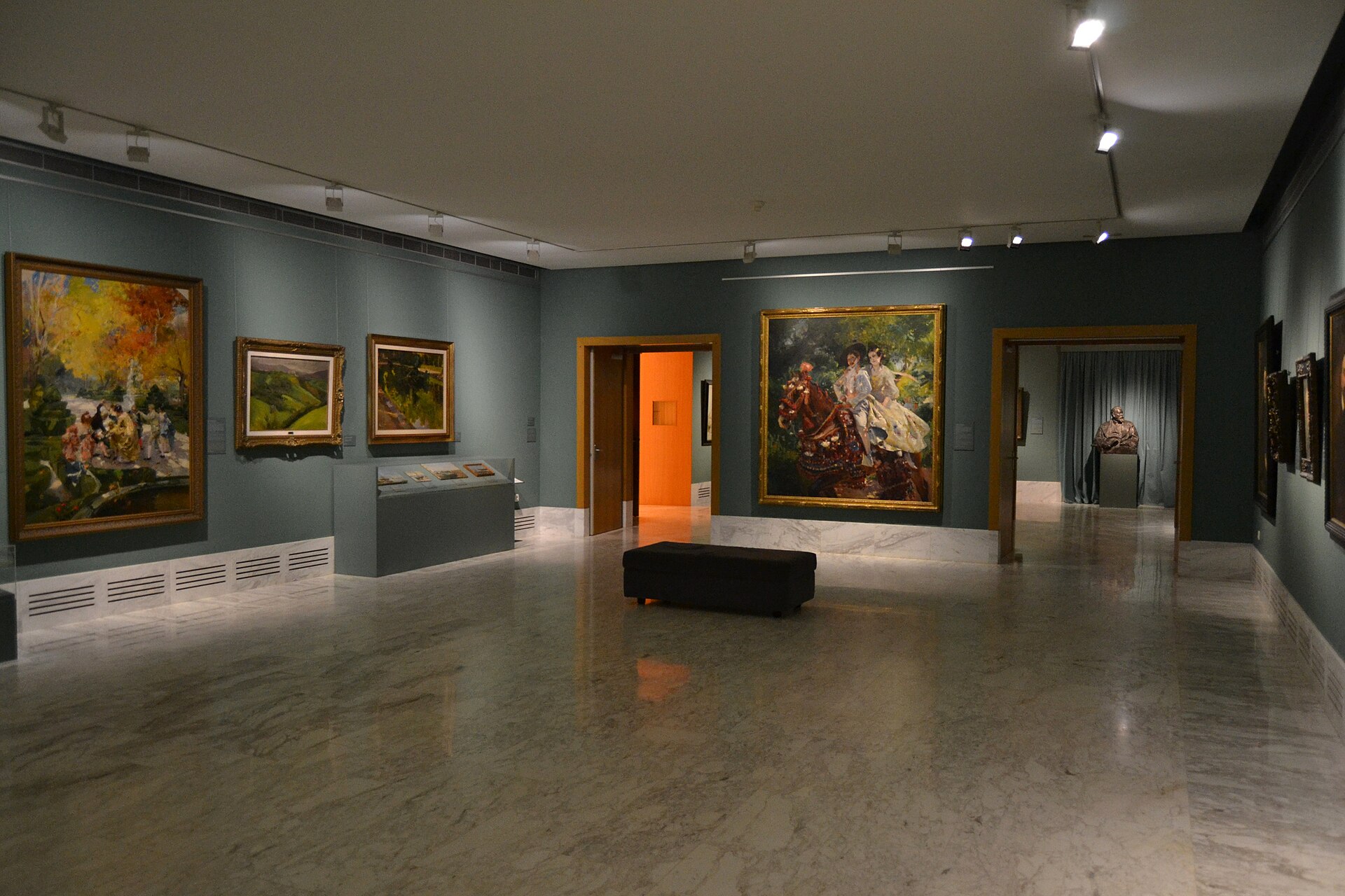 A modern gallery with marble floors and grey walls hung with Impressionist-style paintings including a large canvas of a horse-drawn carriage with two riders