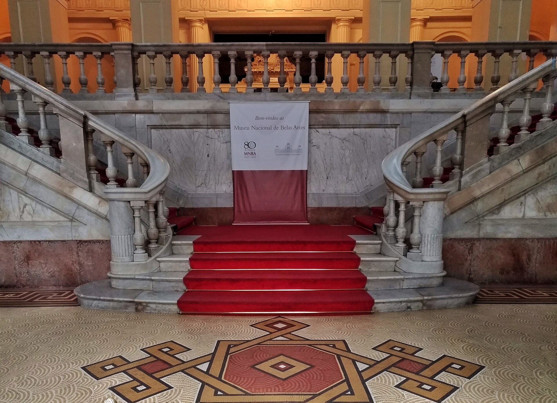 The ground floor entrance hall of the museum, with a welcome banner reading Bem-vindos ao Museu Nacional de Belas Artes and the base of a grand marble staircase beyond a patterned floor
