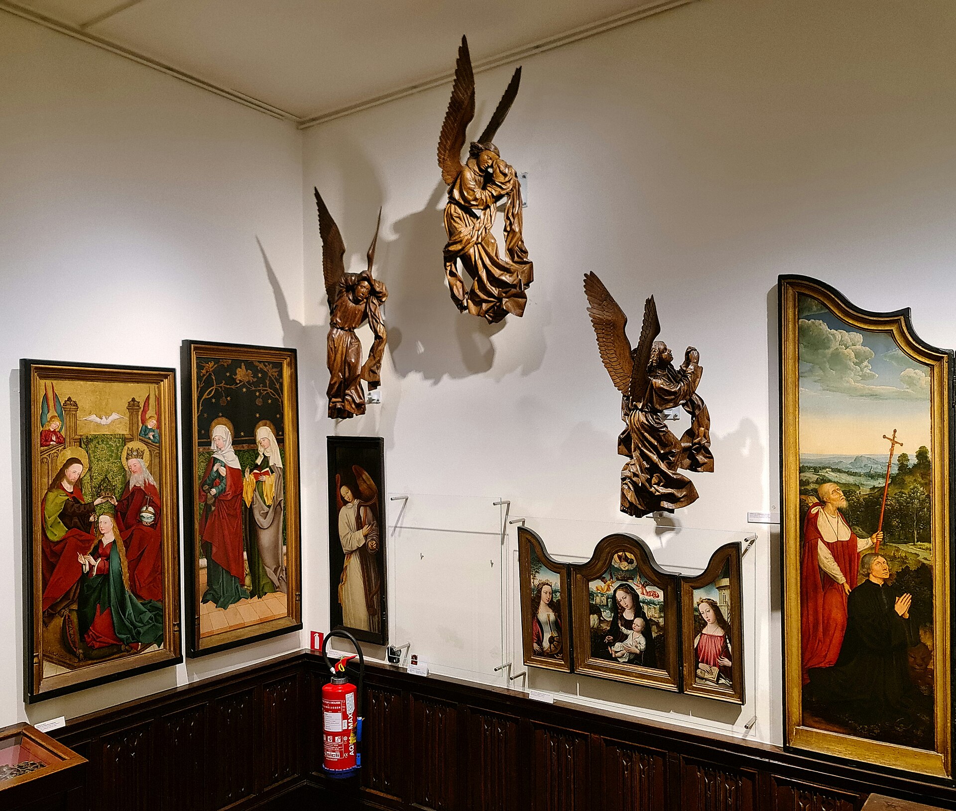 A corner gallery in the museum hung with medieval devotional panel paintings and carved polychrome wooden angel sculptures