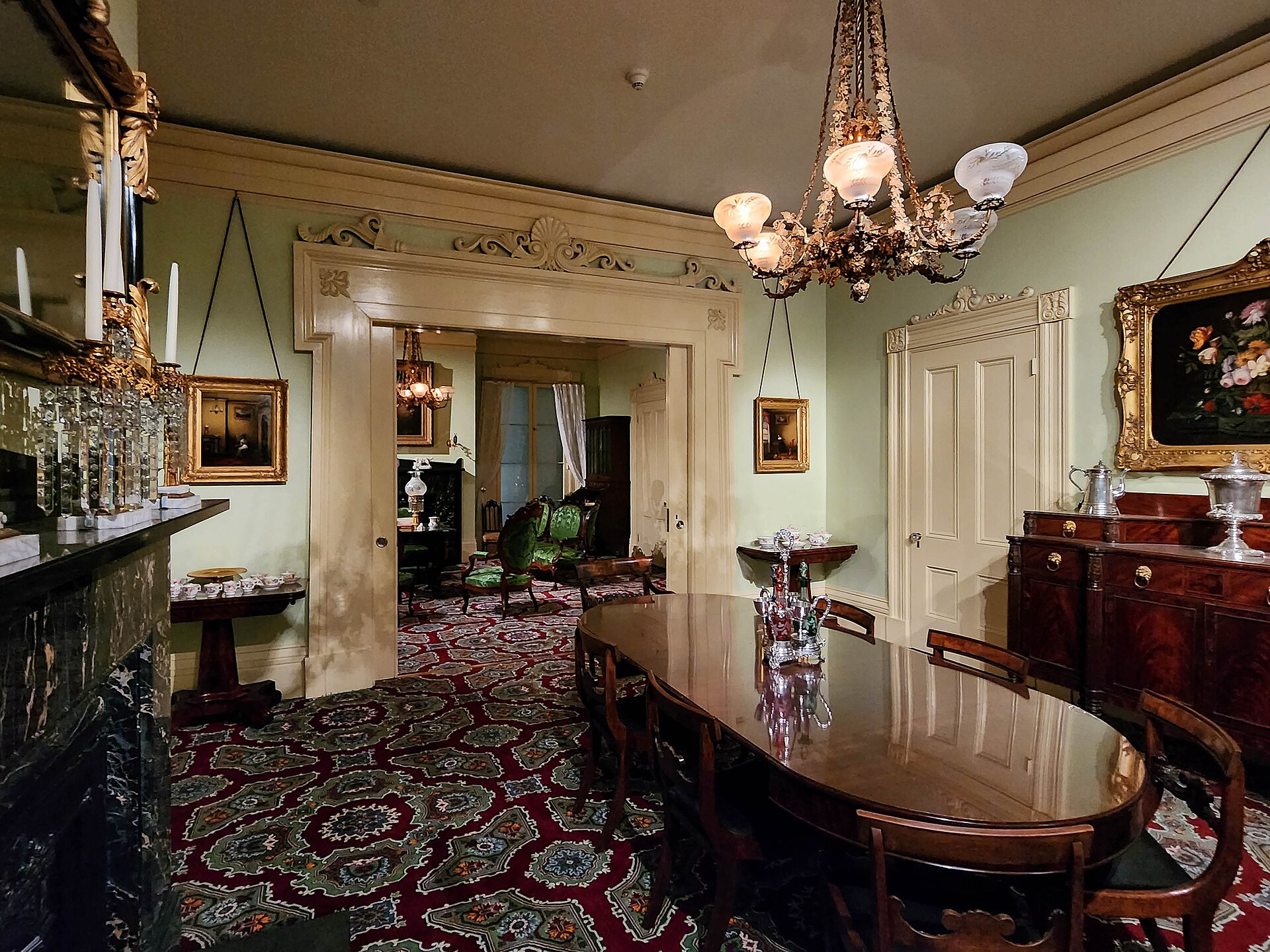 A furnished nineteenth-century American parlor with green wallpaper and a marble-topped sideboard