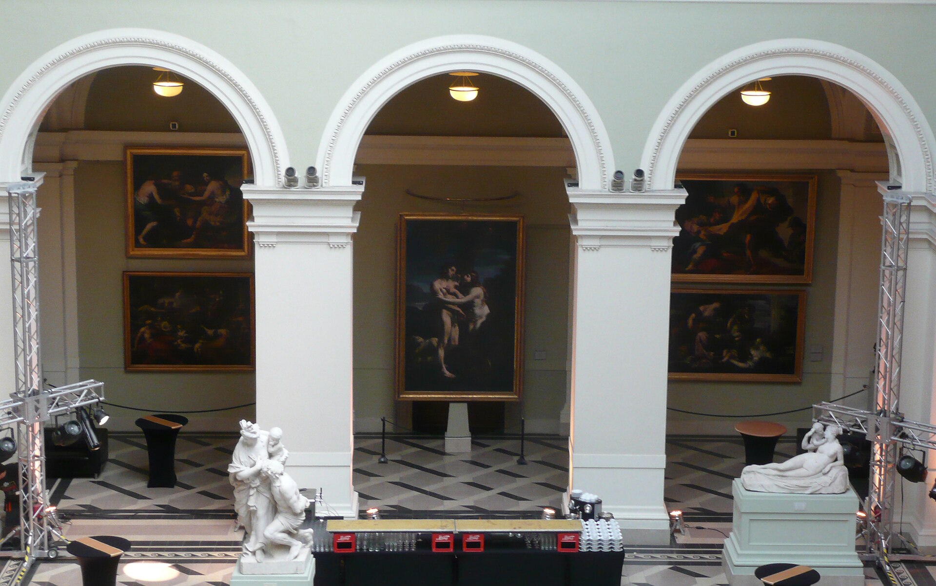 A gallery of Italian old master paintings hung beneath arched openings, with sculpture on plinths in front