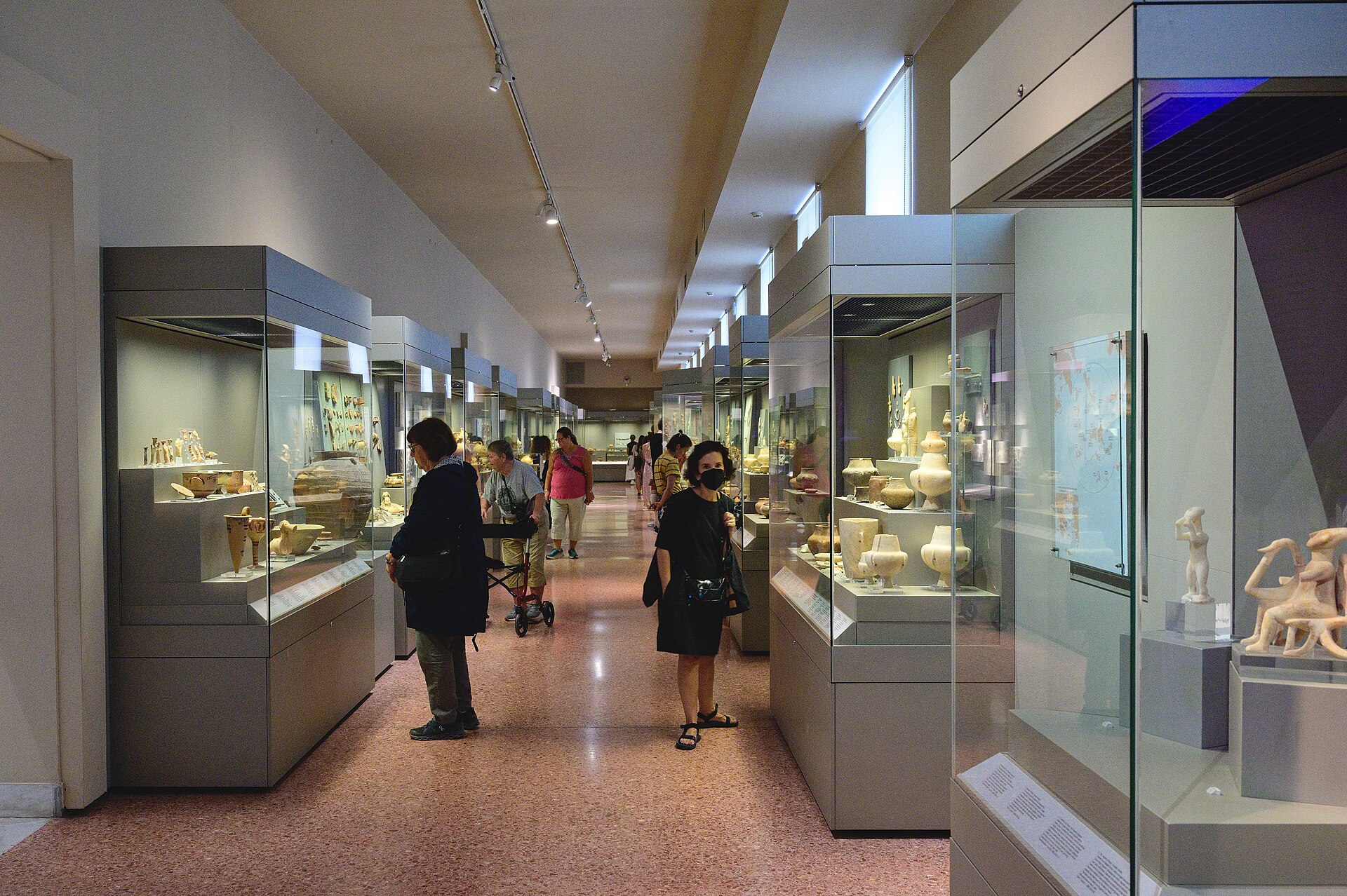A corridor gallery of glass display cases holding white marble Cycladic figurines and vessels