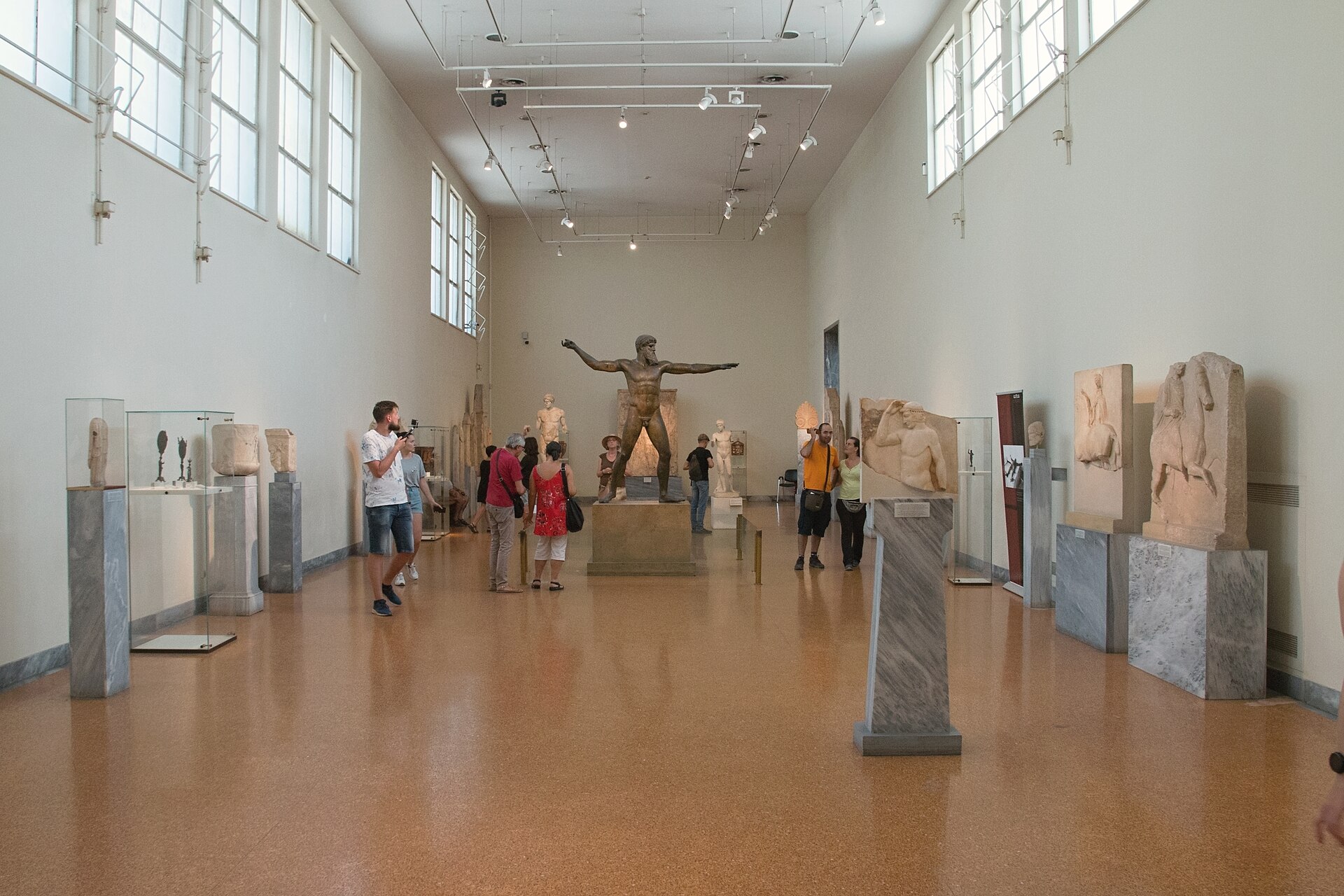 The Room of Poseidon, a long sculpture gallery with the bronze god statue standing at the far end and grave stelai lining both walls