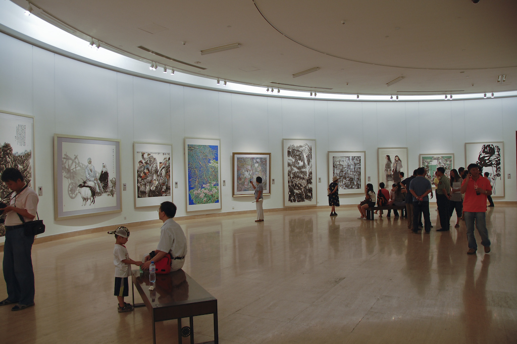 A curved gallery of hanging Chinese ink-painting scrolls at the National Art Museum of China, with visitors viewing the works