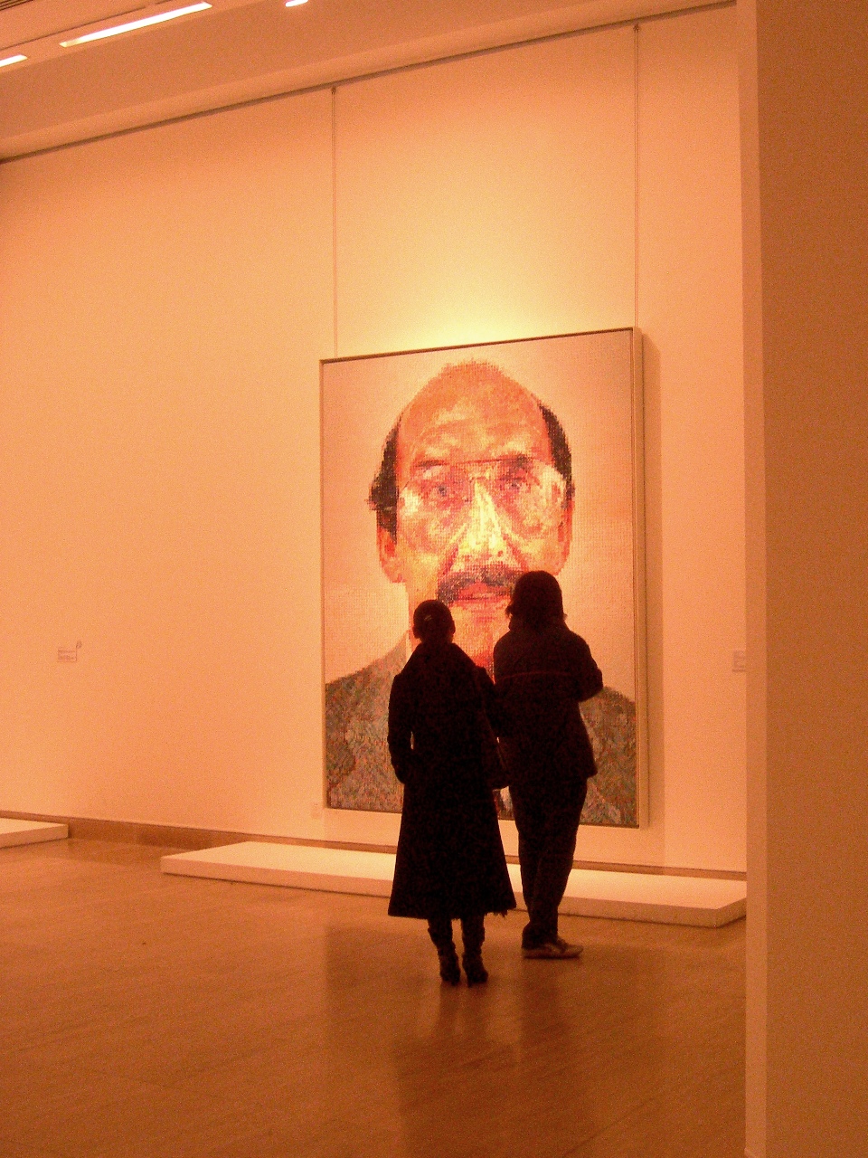 Visitors viewing a large photorealist Western portrait painting in a National Art Museum of China gallery